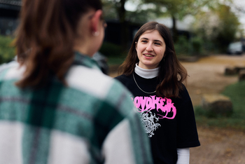 Bild von Maya Chrobok Die Schülerin des Berufskollegs Senne steht in einem schwarzen T Shirt auf dem in rosa Provoker steht auf dem Schulhof der Schule Sie hat lange braune Haare und ein schmales Gesicht